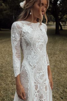 a woman wearing a white lace dress and flower in her hair, standing on the grass