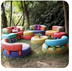 an outdoor seating area with colorful tires and cushions on the grass, surrounded by trees