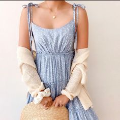 a woman in a blue dress holding a straw hat with her hands behind her back