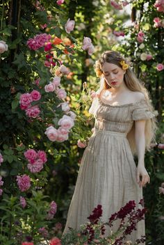 a woman in a white dress standing next to pink and red flowers with her hands on her hips