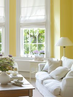 a living room with yellow walls, white furniture and flowers in vases on the coffee table