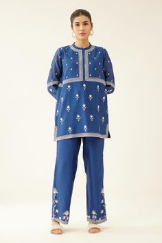 Blue short kurta with silk thread embroidery in floral pattern and round neckline. Paired with straight pant.
Components: 2
Pattern: Embroidery
Type Of Work: Thread, floral
Neckline: Round
Sleeve Type: Three quarter
Fabric: Silk Chanderi
Color: Blue
Other Details: 
Lined
Embroidery on pant hem
Elasticated waist at the back
Side pockets
Closure: Pant: Drawstring
Occasion: Work - Aza Fashions Indigo Chikankari Embroidery Sets For Navratri, Indigo Chikankari Sets For Navratri, Indigo Embroidered Sets For Navratri, Festive Blue Embroidered Pant Set, Festive Embroidered Blue Pant Set, Blue Pant Set With Resham Embroidery, Traditional Blue Pant Set With Floral Embroidery, Traditional Blue Pants For Festive Occasions, Traditional Blue Pants For Festive Season