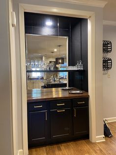 a kitchen with black cabinets and wooden counter tops in an open doorway to the living room