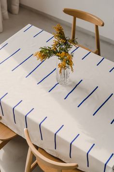 a vase with some flowers on top of a white table cloth that has blue lines drawn across it