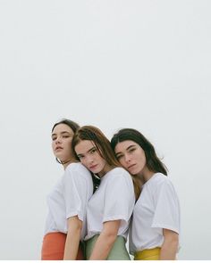 three young women standing next to each other in front of a white wall and looking at the camera