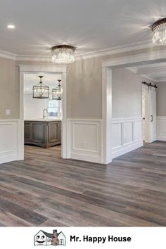 an empty living room with hard wood flooring and white paint on the walls, along with chandeliers