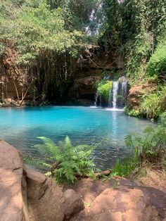 there is a blue pool in the middle of some rocks and trees with water running down it