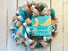 a wreath made out of burlocks and ribbons with the words mermaid crossing on it