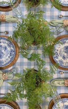 the table is set with blue and white plates, silverware, ferns and candlesticks