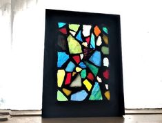 a colorful stained glass window sitting on top of a wooden table next to a white wall