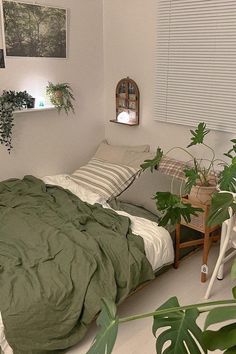 a bed with green sheets and pillows in a white room next to some potted plants