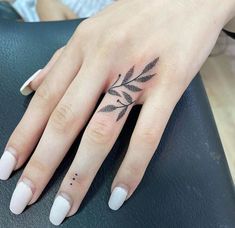 a woman's hand with a small black leaf tattoo on her left ring finger