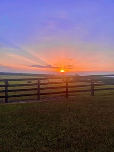 the sun is setting behind a fence in an open field