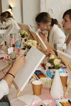 a group of people sitting around a table with easels and flowers on it,