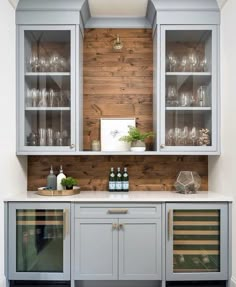 a kitchen with gray cabinets and wine glasses on the top shelf, along with other glassware