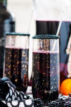 two glasses filled with liquid sitting on top of a table next to oranges and blackberries