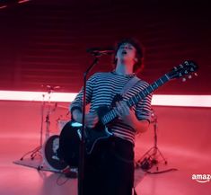 a young man playing guitar in front of a microphone and drums on a red background