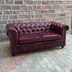 a red leather couch sitting on top of a brick floor next to a stone wall