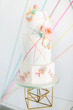 a three tiered cake with geometric designs and flowers on the top is sitting on a gold stand