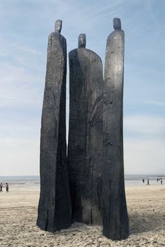 two large black sculptures sitting on top of a sandy beach