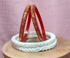 two red and gold bracelets sitting on top of a wooden stand