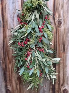 a wreath hanging on the side of a wooden fence with red berries and green leaves