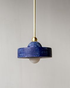 a blue lamp hanging from a gold colored light fixture with a white wall in the background