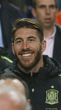 a man with a goatee smiles while sitting in front of other men at a sporting event