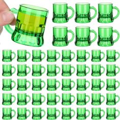 a hand holding a green glass mug next to a set of coffee cups with handles