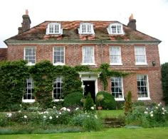 a large brick building with white windows and ivy growing on it's sides in front of a lush green lawn