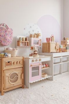 a toy kitchen with pink appliances and white carpeted flooring in a child's room