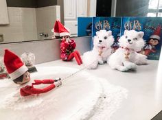 two elf dolls sitting on top of a bathroom counter next to stuffed animals and books