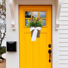 a yellow door with a white bow and flowers in the pot hanging on it's side