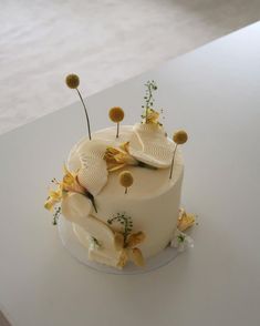 a white cake with yellow flowers and leaves on it's top is sitting on a table