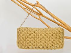 a crocheted purse hanging from a wooden branch with some branches in the background