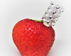 a close up of a strawberry with a diamond ring on it's end, against a white background