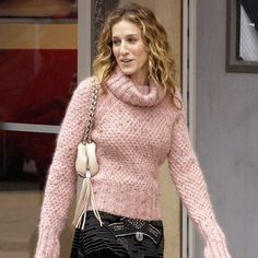 a woman in pink sweater and black pants walking down the street with her hand on her hip