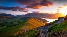 a person standing on top of a lush green hillside next to a lake at sunset