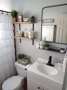 a white toilet sitting under a bathroom mirror next to a sink and a shower curtain