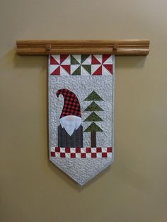 a quilted banner hanging on the wall with a gnome's hat and trees