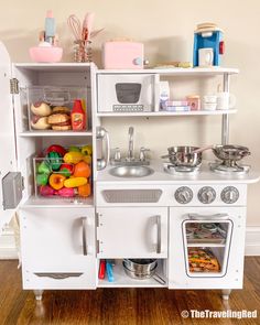 a white toy kitchen with lots of food in it's cupboards and shelves