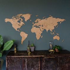 a wooden world map mounted on the wall above a dresser with potted plants next to it