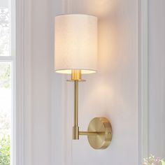 a wall light with a white shade on it's side in front of a window