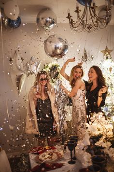 three women standing in front of a mirror with confetti falling from the ceiling