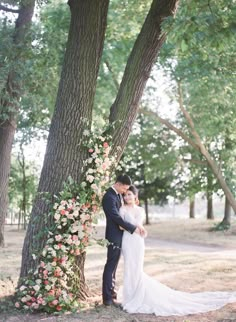 a bride and groom standing in front of a tree with flowers on the branches at their wedding