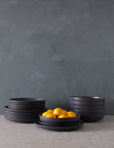 black bowls with oranges in them sit on a table next to a gray wall