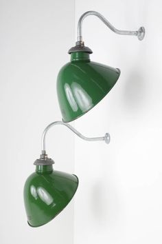 two green lamps hanging from the side of a wall next to each other on a white background