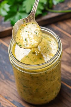 a spoon full of pesto sauce sitting on top of a wooden table next to parsley