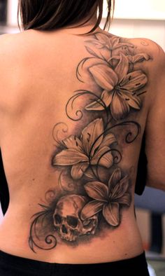 a woman's back with flowers and a skull tattoo on her left side ribcage