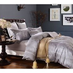 a bed with grey and gold comforters in a room next to pictures on the wall